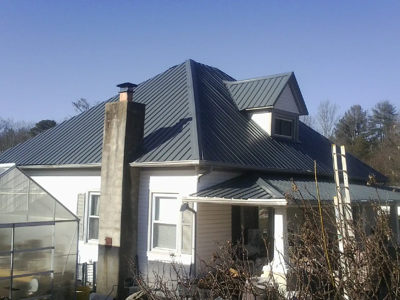 Dark blue standing seam metal roof on a white farmhouse with dormer — Slate & Tile Roof Repair by Roofing Brothers in Manorville