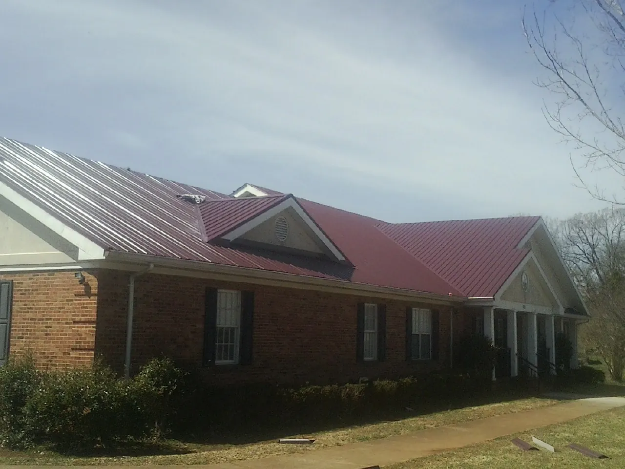 Red metal roof with gabled entries on a long brick building, from a Hail Damage Roof Repair job in Manorville