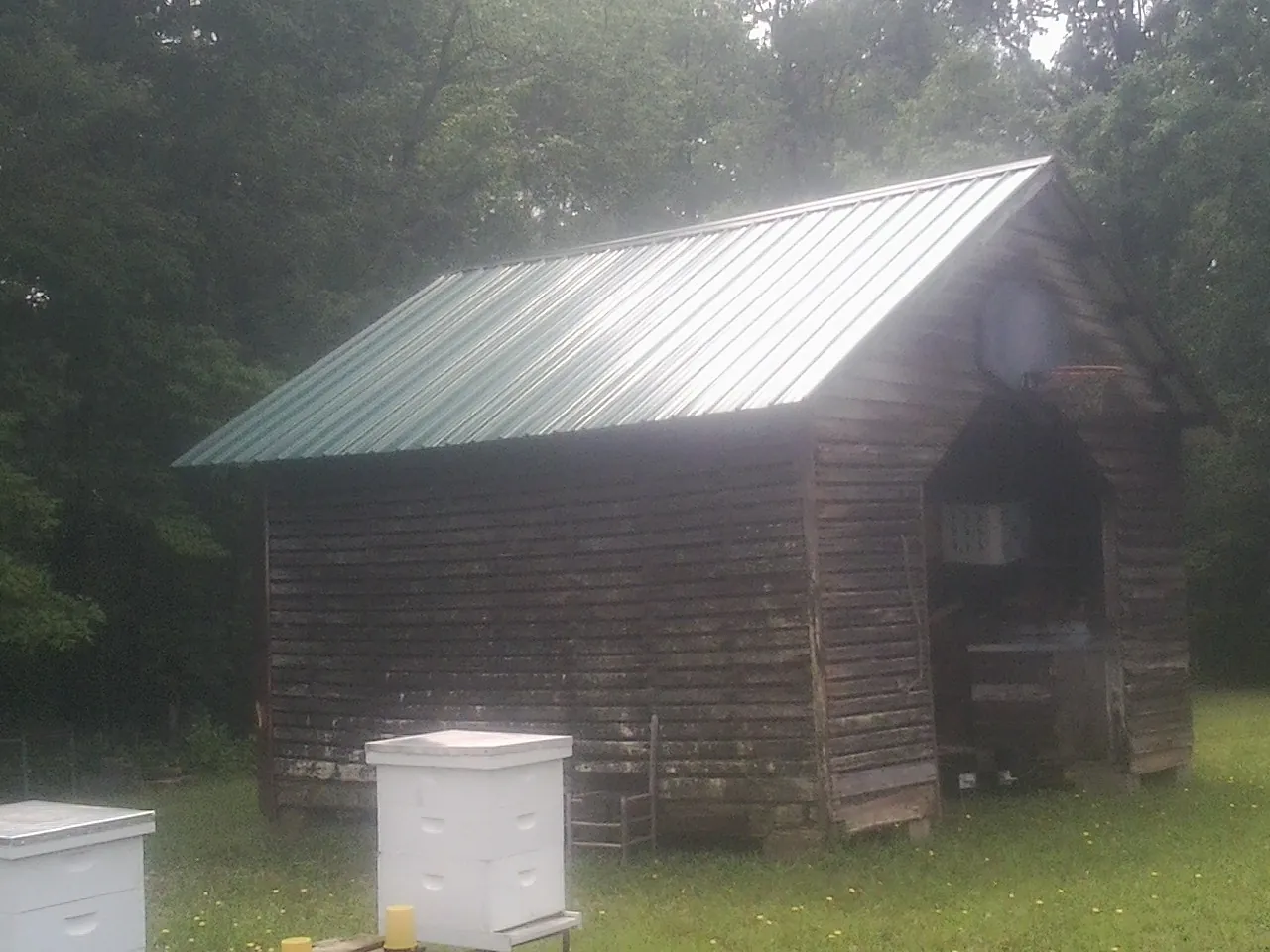 Green metal roof on a weathered barn beside stacked beehives in Manorville