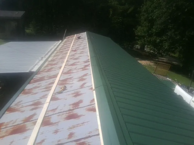 Old rusted panels beside newly installed green metal roofing — Wind Damage Roof Repair by Roofing Brothers in Manorville