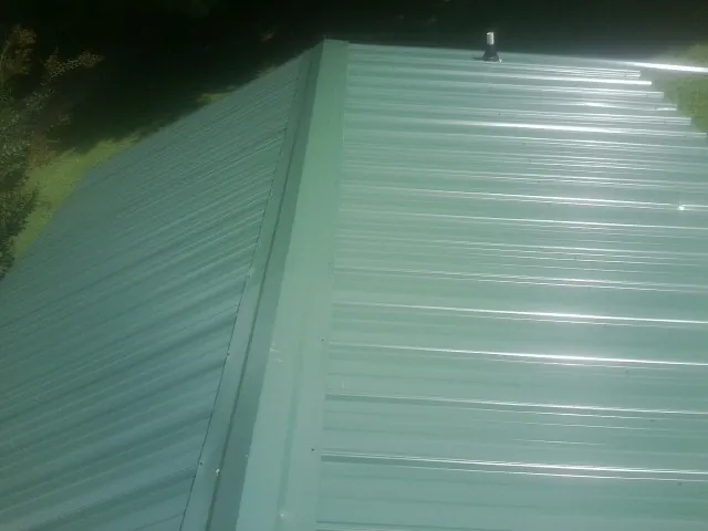 New green metal panels meeting at the ridge of a roof — Flat Roof Repair work by our crew in Manorville