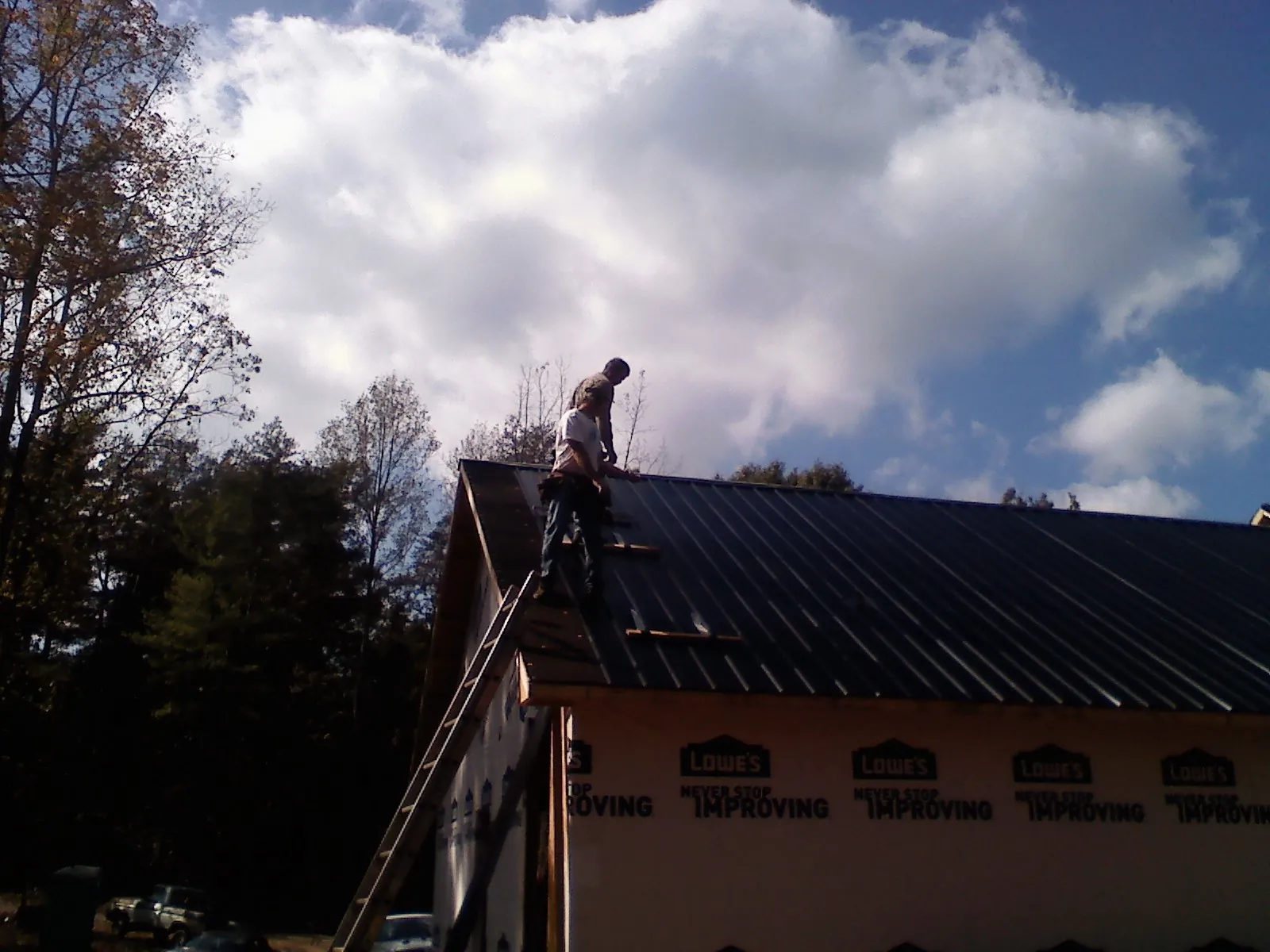 Roofer fastening dark metal panels high against a cloudy sky, from a Roof Inspection job in Manorville