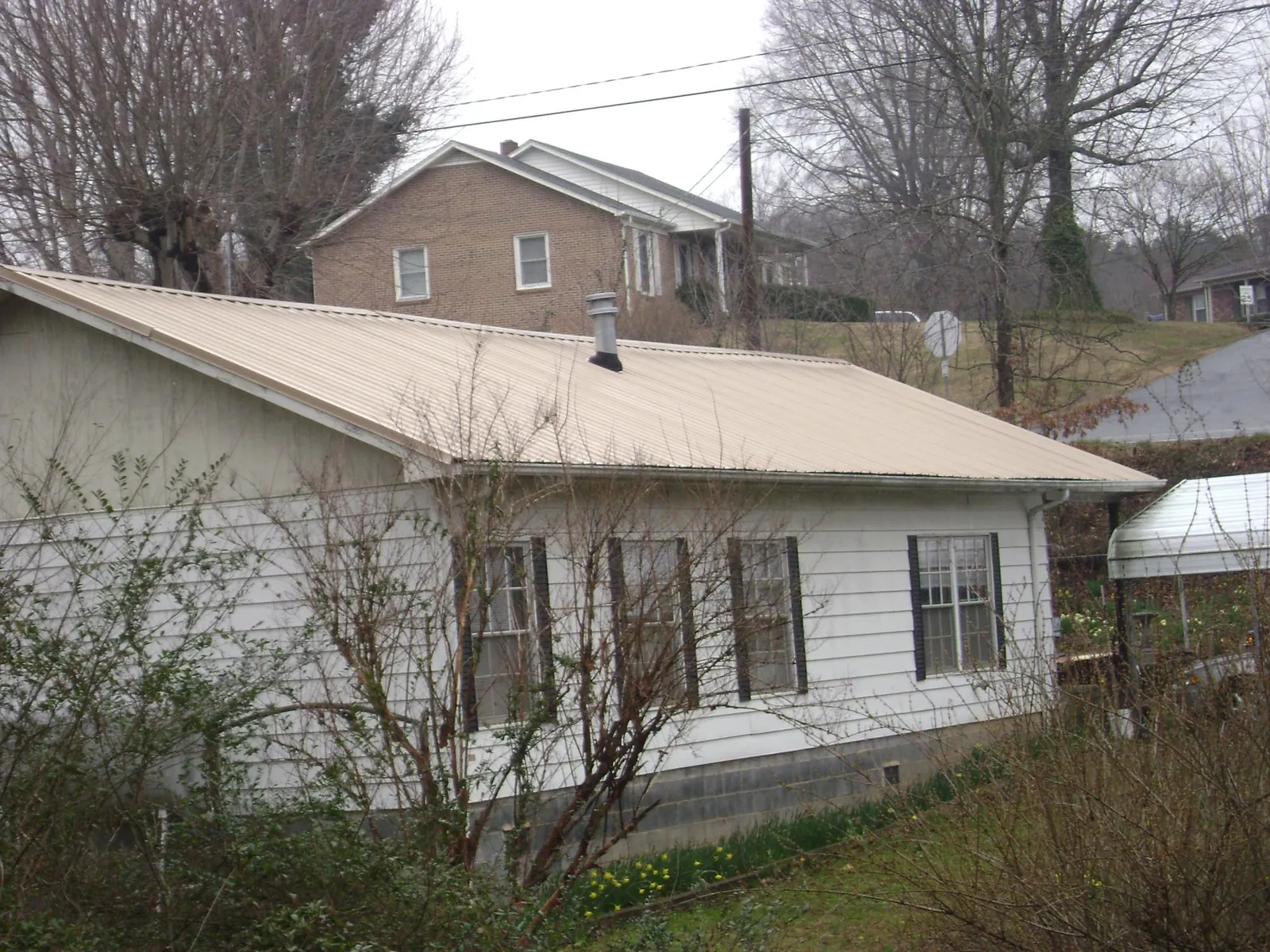 Tan metal roof on a white sided house set into a hillside — Commercial Roofing by Roofing Brothers in Manorville