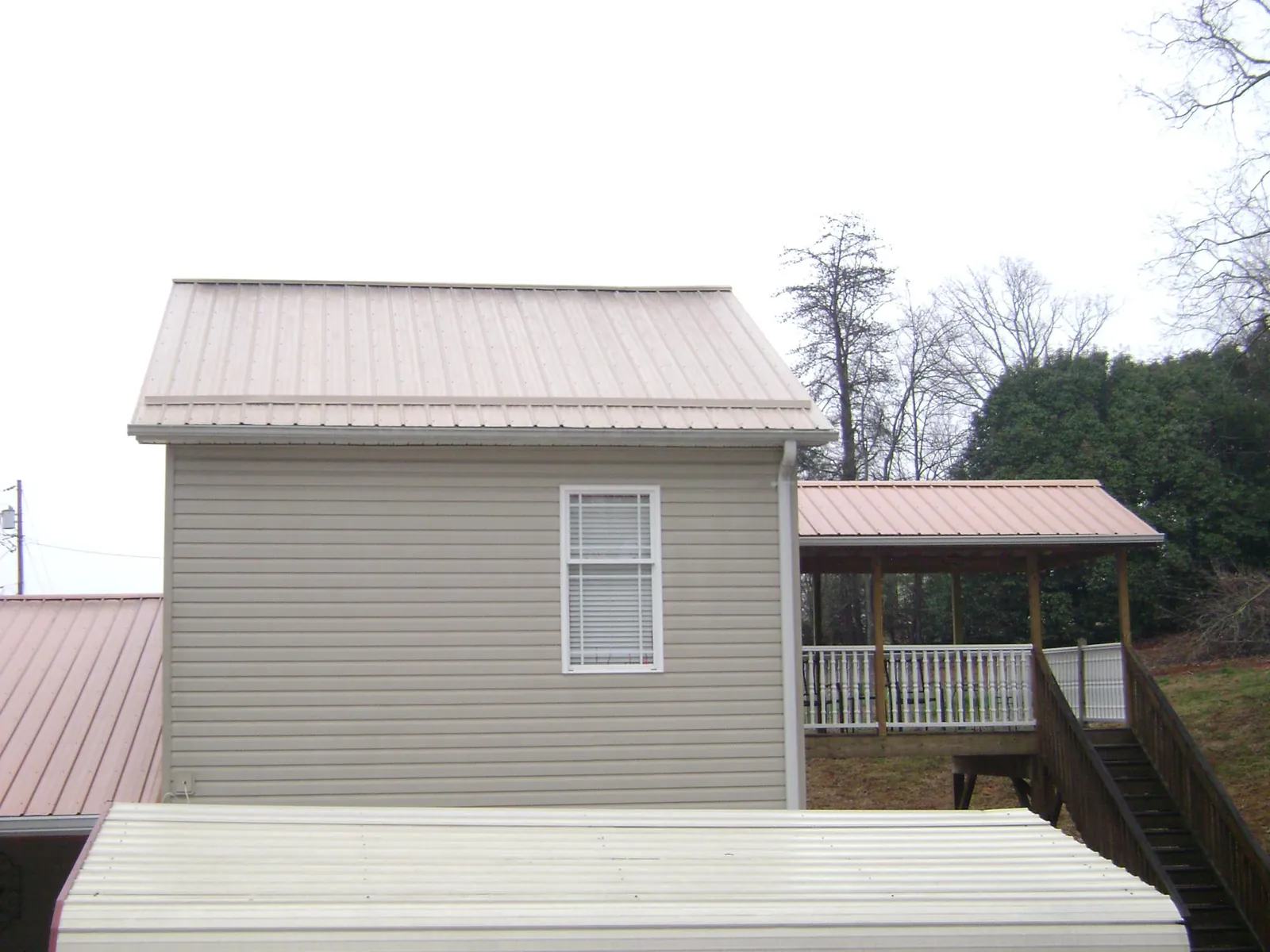 Tan metal roofs on a two story addition and attached porch, from a Roof Replacement job in Manorville